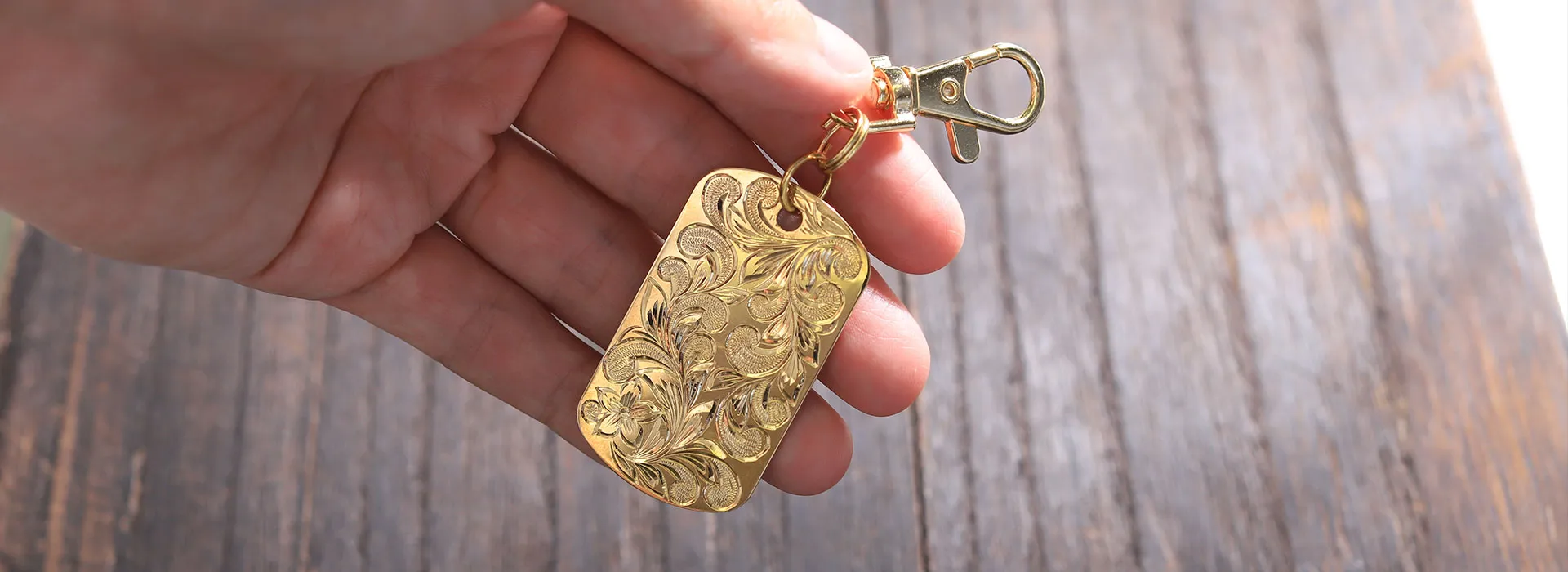 手に持った、彫りの入った金色のプレートのキーホルダー