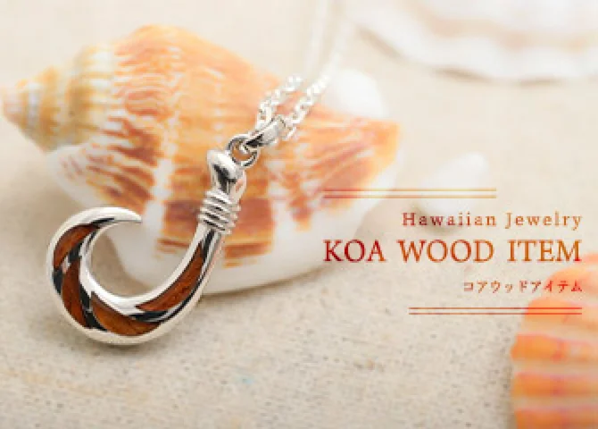 貝殻の前に置いた、コアウッドを入れたフィッシュフックのネックレス。「Hawaiian Jewelry KOA WOOD ITEM コアウッドアイテム」の文字入り