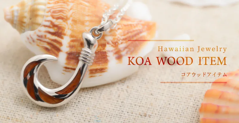 貝殻の前に置いた、コアウッドを入れたフィッシュフックのネックレス。「Hawaiian Jewelry KOA WOOD ITEM コアウッドアイテム」の文字入り